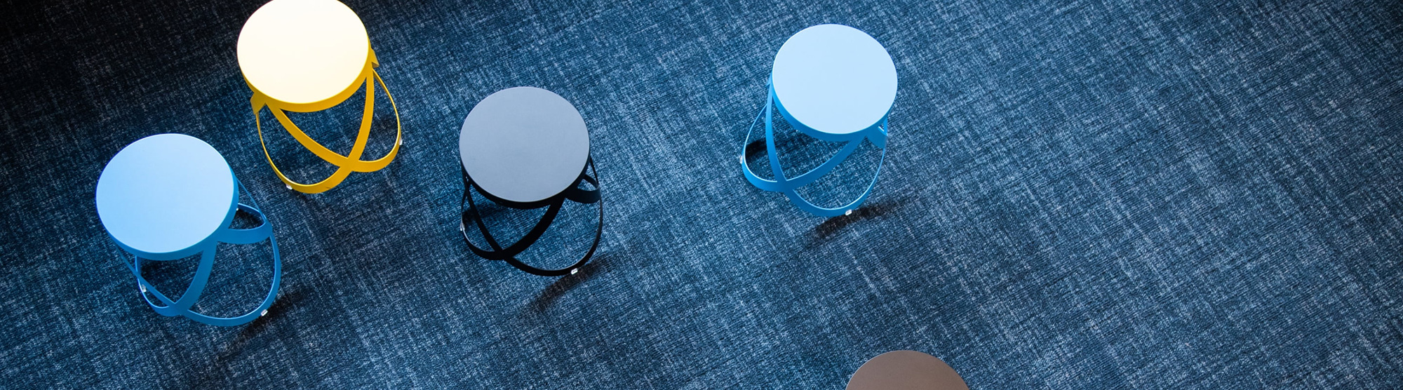 Ein blauer Teppich mit vier Hockern in weiß und verschiedenen Blautönen darauf verteilt.
